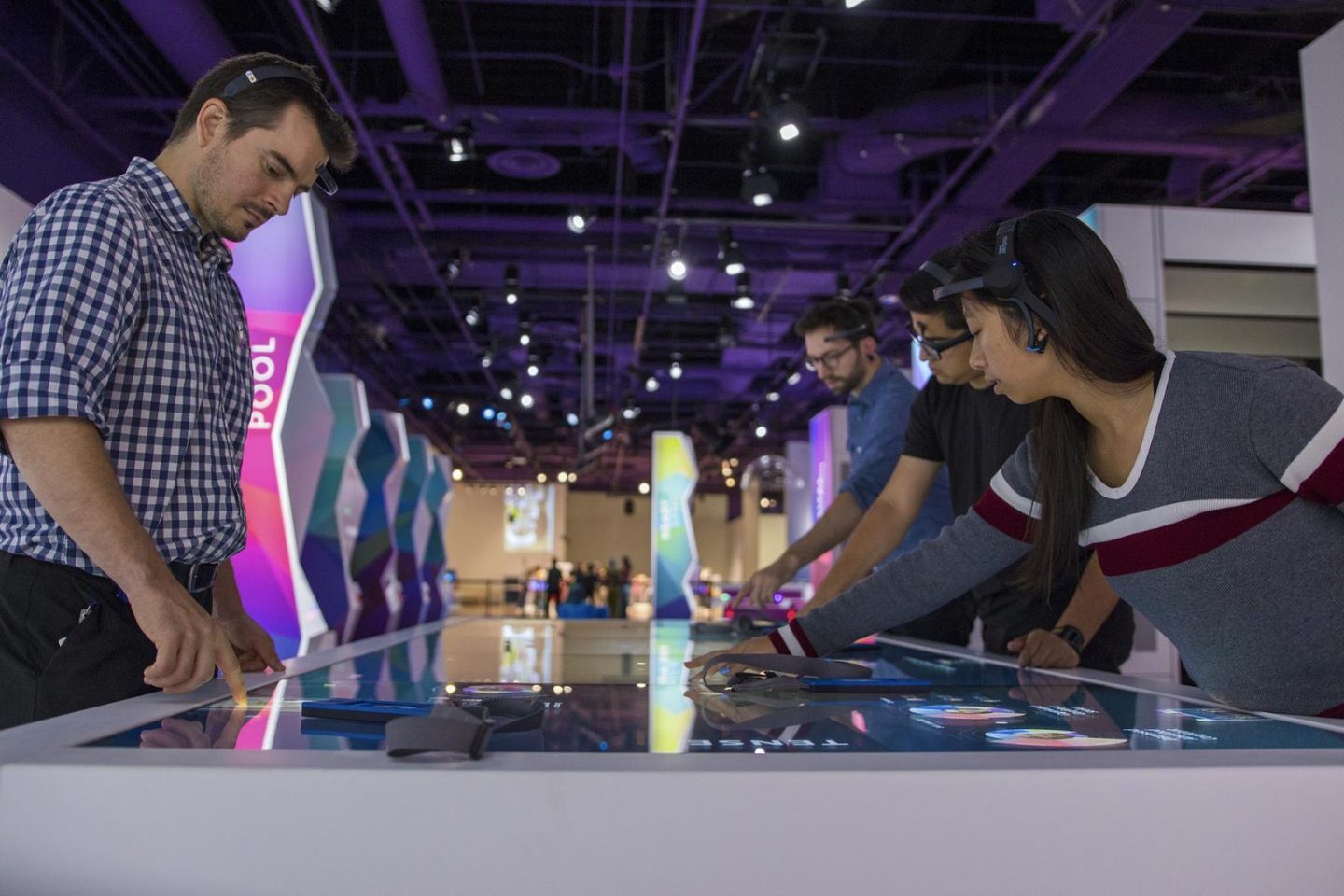 A visitor at a Body Metrics interactive station, hands resting on a sensor surface as a wall-scale visualization renders their physiological signal in flowing patterns of color.